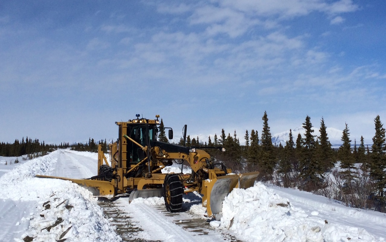 Snow plow pushes snow off road against blue sky