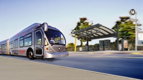 Silver bus moves near bus stop