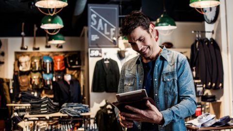 A man in a retail store holds a smart device.