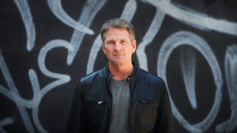 Doug Stephens, founder of Retail Prophet, stands against a backdrop of white painted graffiti on a black background.