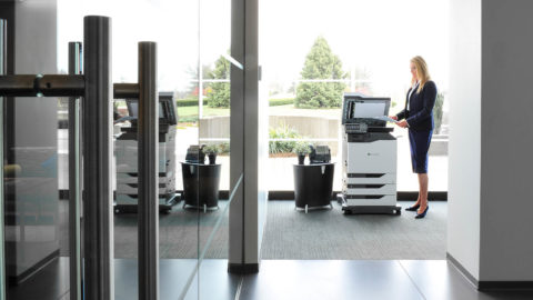 Woman in business attire stands near a printer in an office