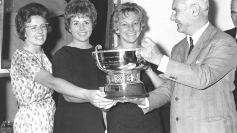 A black-and-white photo shows three women's tennis champions smiling as they accept a trophy for winning the 1963 Fed Cup