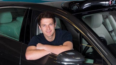 A man sits inside a car, looking out through the side window with his arms folded on the door frame.