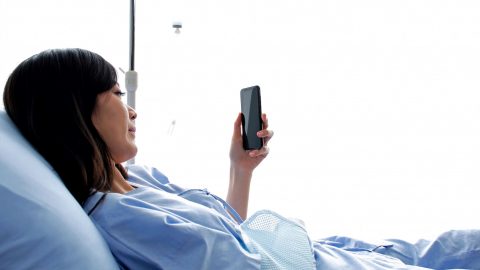 A woman in a hospital bed holds a mobile phone