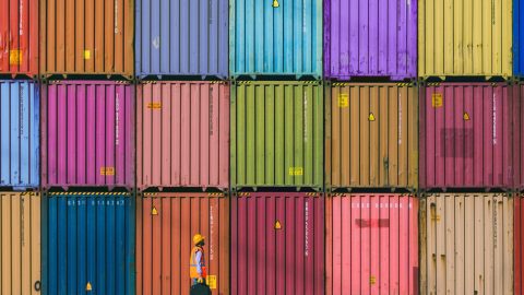 A male worker in front of stacks of shipping containers