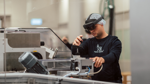 A technician at a Novo Nordisk production facility uses the HoloLens 2 with augmented instructors to make adjustments to a machine.