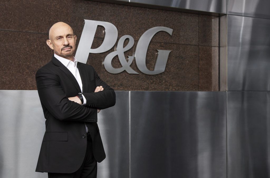 Vittorio Cretella stands with arms folded in front of a wall that shows the P&G logo.