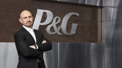 Vittorio Cretella stands with arms folded in front of a wall that shows the P&G logo.