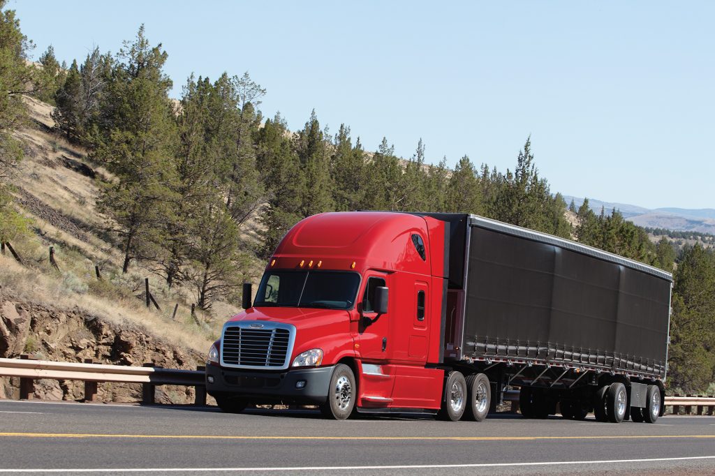 Photo of a red semi truck on a highway lined with trees.