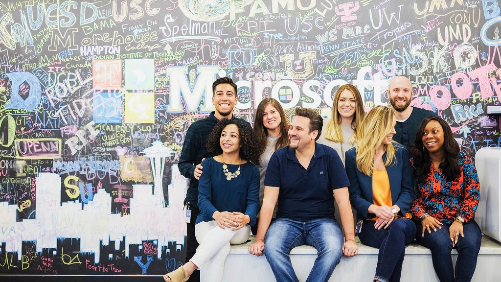 A group of employees sitting in front of a graffiti wall that says Microsoft