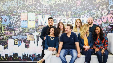 A group of employees sitting in front of a graffiti wall that says Microsoft