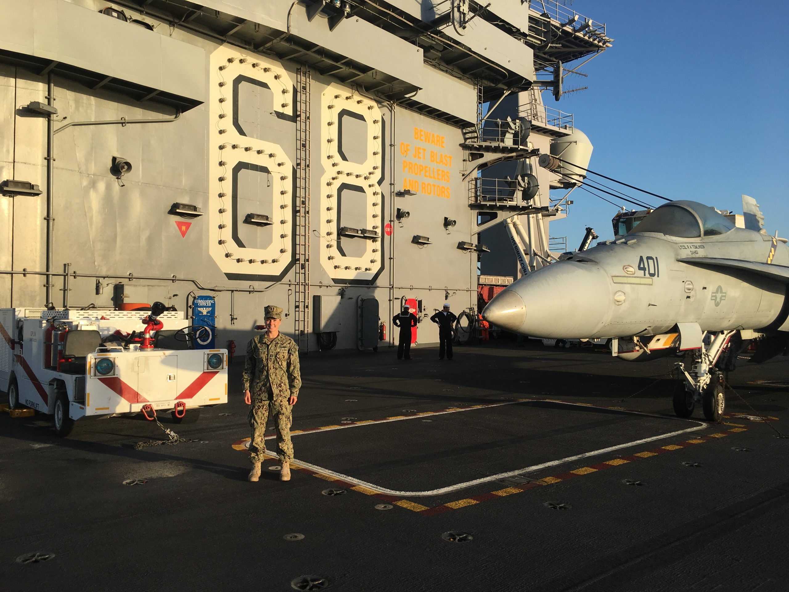 woman in camos standing on the deck of a ship with airplane behind her