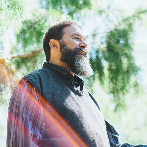 A photo of a Microsoft employee smiling while standing under trees and sunshine