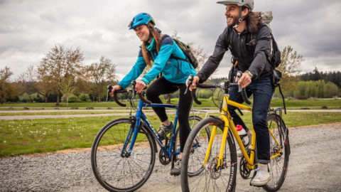 A man and a woman each ride a bike on a gravel trail