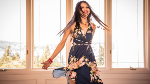 A woman in a black dress twirls in front of a window