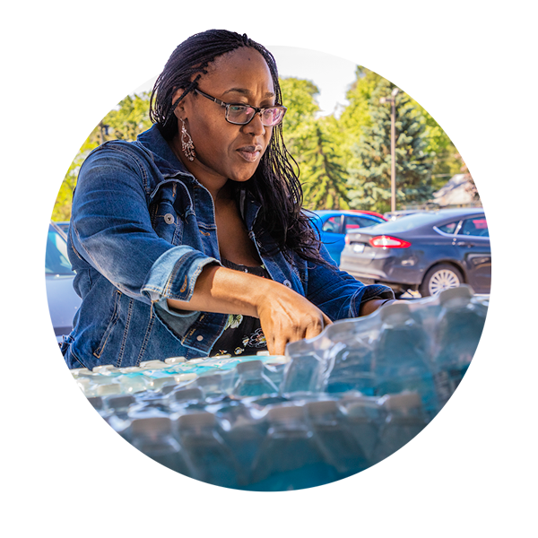 A woman leans over to pick up a package of bottled water