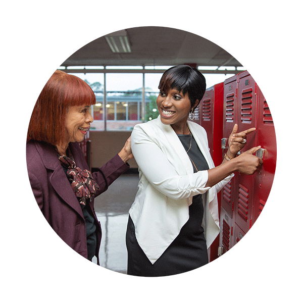 Two women smile at each other standing in front of old school lockers
