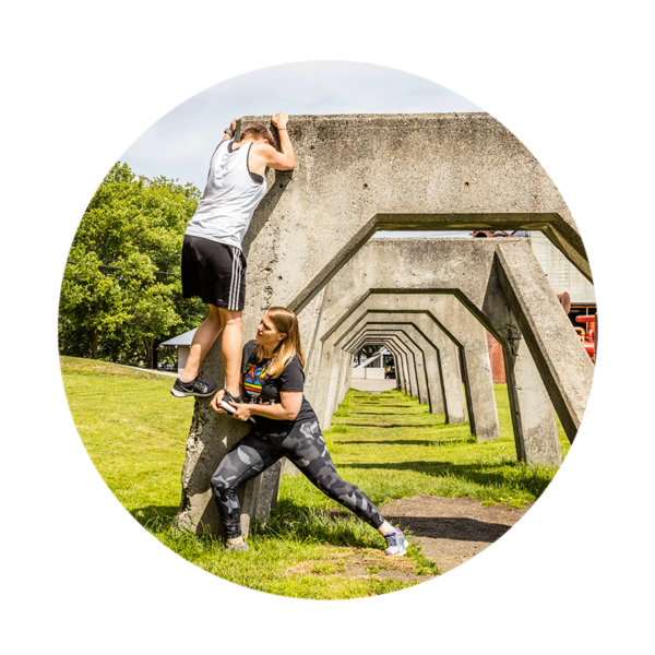 A woman holds up another woman's foot to climb a stone structure