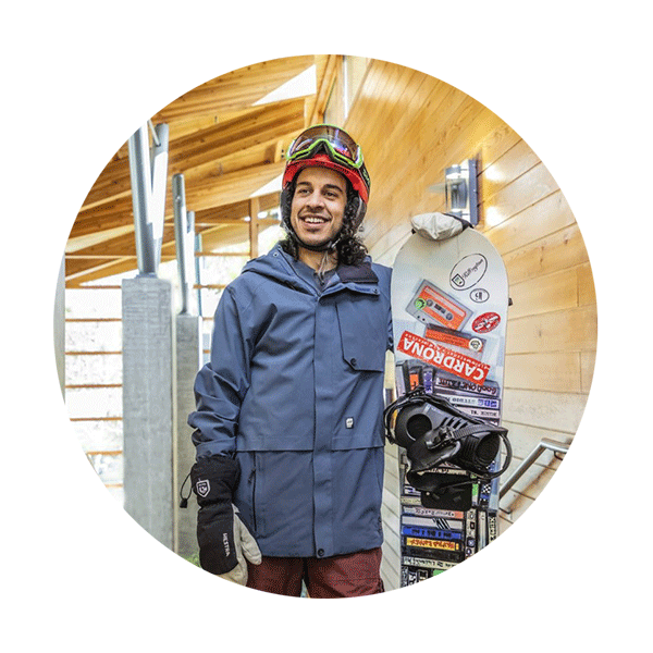 a man smiling while holding a snowboard and wearing a heavy coat and snow mask