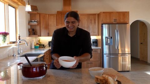 A man serving a bowl of chile in his kitchen