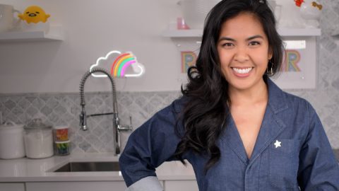 A woman in a woman smiling as she stands in front of a kitchen sink
