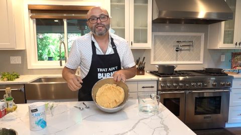 A man wearing an apron holds a pan of dough