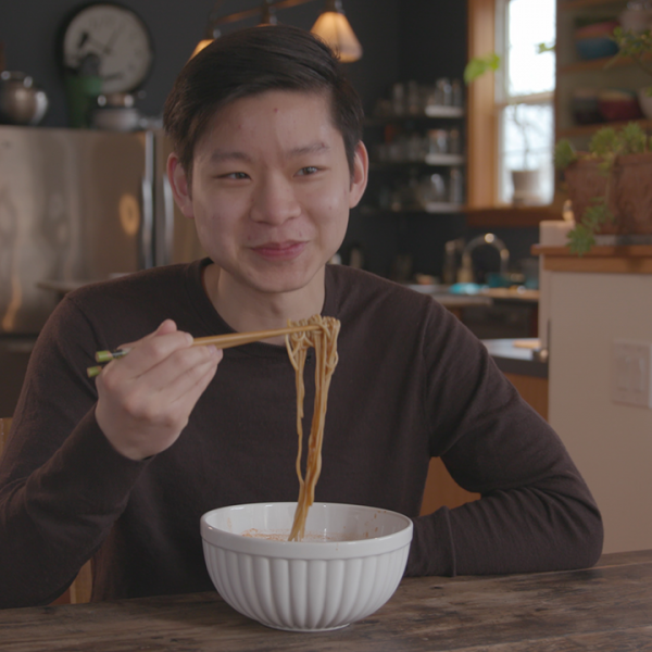 A man eats beef noodle soup using chop sticks