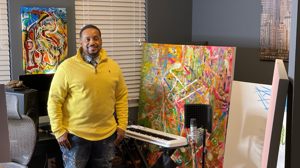 A photo of a man standing next to an art painting and a piano keyboard