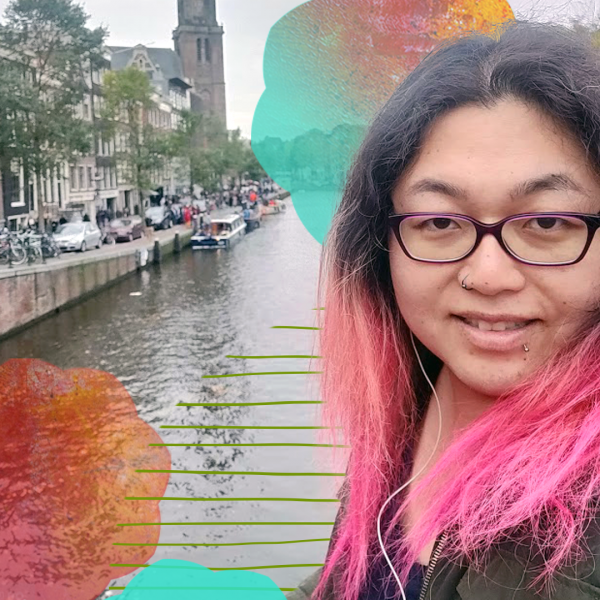 A woman with pink hair and glasses standing in front of a river