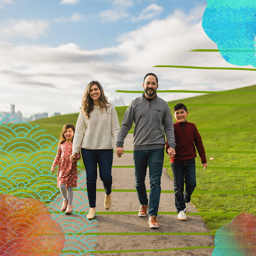 a man, woman, and two children hold hands while walking through a park