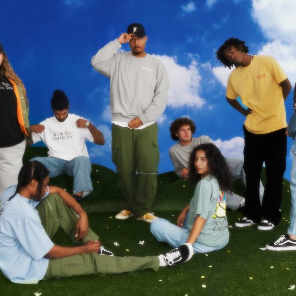 Group of eight people wearing Hardwear clothing, sitting and standing on grass, in front of a blue and white background.