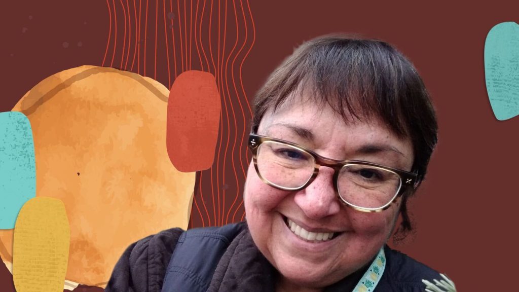 Deanna wearing a black jacket and smiling in front of a brown background with colorful hues.