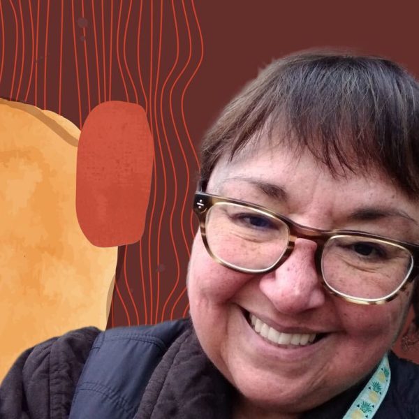 Deanna wearing a black jacket and smiling in front of a brown background with colorful hues.