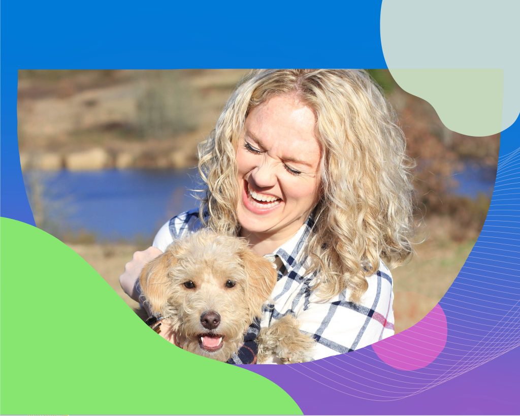 Naomi outside, sitting. Her small curly haired dog is on her lap. She's smiling joyfully.