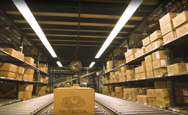 Das Foto zeigt ein Band im Lager von Fruit of the Loom, auf dem ein Versandkarton transportiert wird.