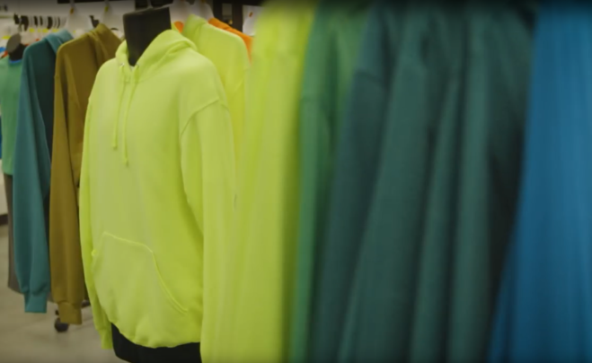 Das Bild zeigt verschiedene Fleece-Jacken von Fruit of the Loom, die teilweise auf einer Kleiderpuppe und teilweise auf Kleiderbügeln hängen. Die dominierenden Farben sind gelb, grün und blau.