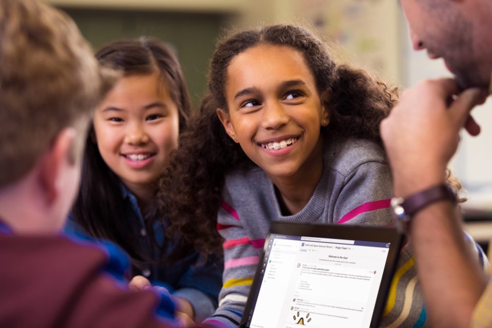 Das Bild zeigt eine Gruppe von jungen Schülerinnen und Schülern, die um ein Laptop gruppiert sind.