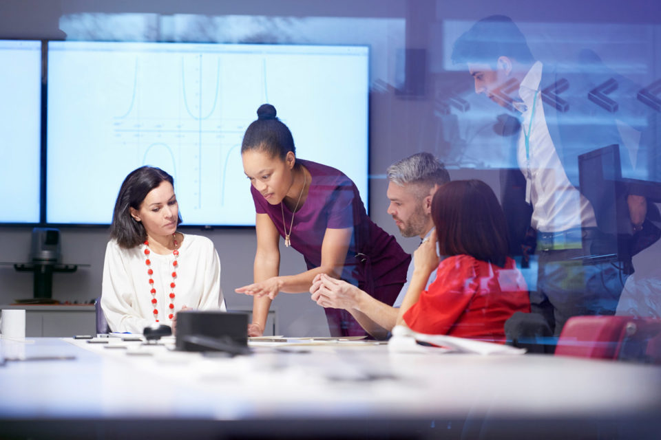 Eine Gruppe von Kolleg*innen sitzen an einem Tisch und schauen gemeinsam auf ein Surface Device.