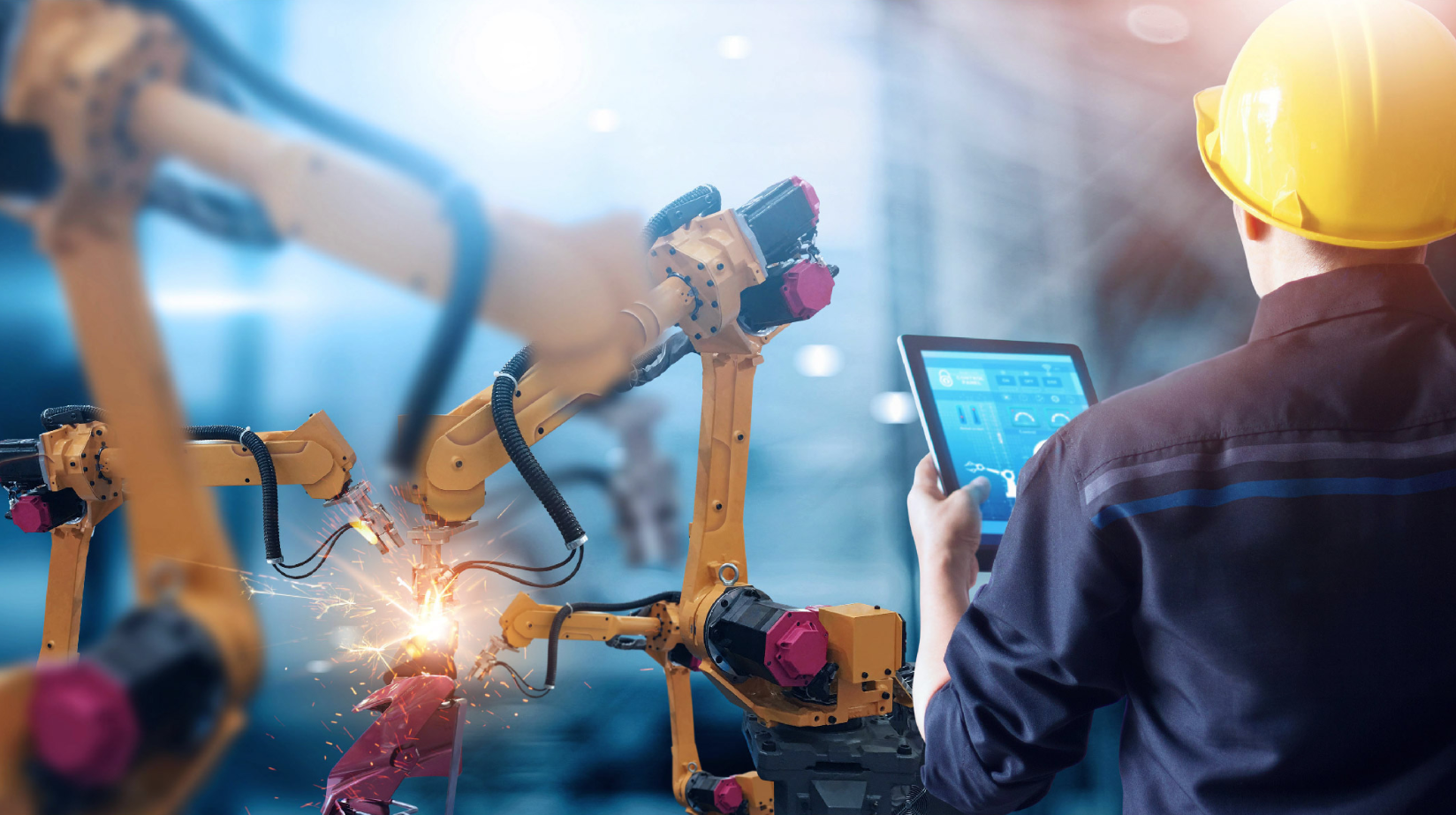 Arbeiter mit Laptop vor einer Fertigungsanlage und Schweißroboter