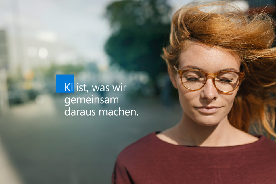 Frau mit wehenden roten Haaren und geschlossenen Augen plus Schriftzug "KI ist, was wir gemeinsam daraus machen"