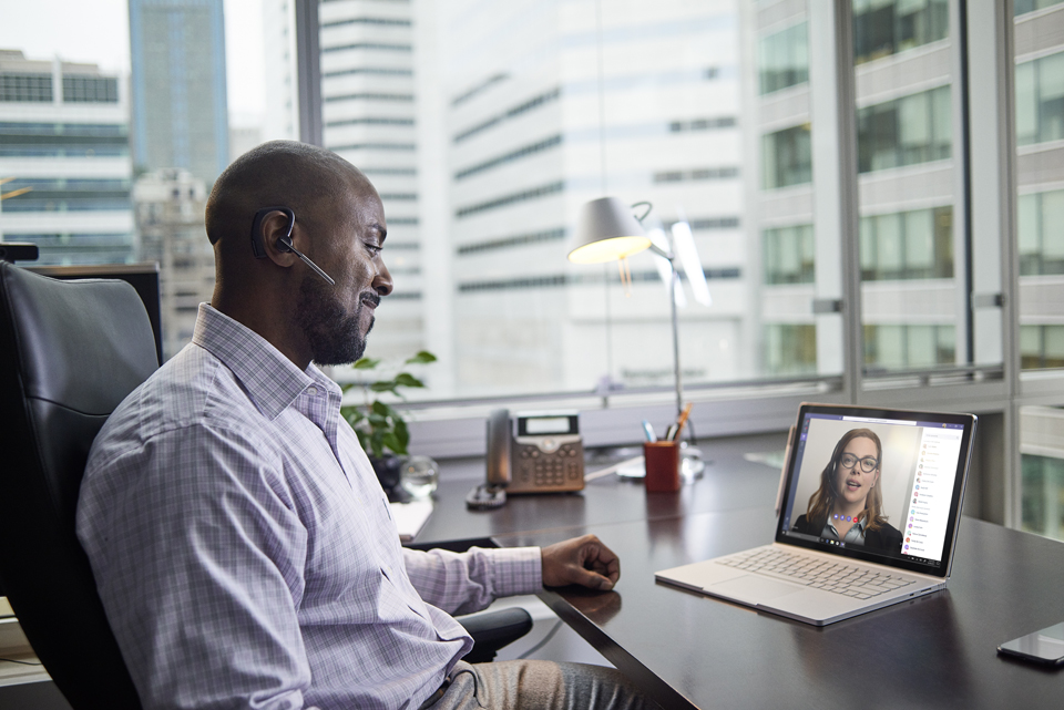 Ein Mann sitzt an seinem Schreibtisch im Büro und hält eine Videobesprechung mit einer Kollegin über Microsoft Teams.