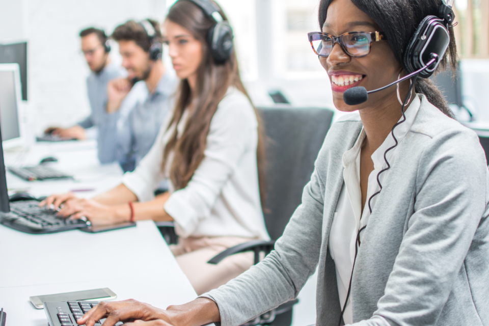 Frau sitzt am Monitor und telefoniert über ein Headset.