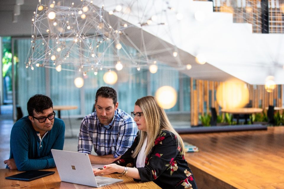 Eine Gruppe von Mitarbeitern sitzt zusammen an einem Tisch vor dem Laptop