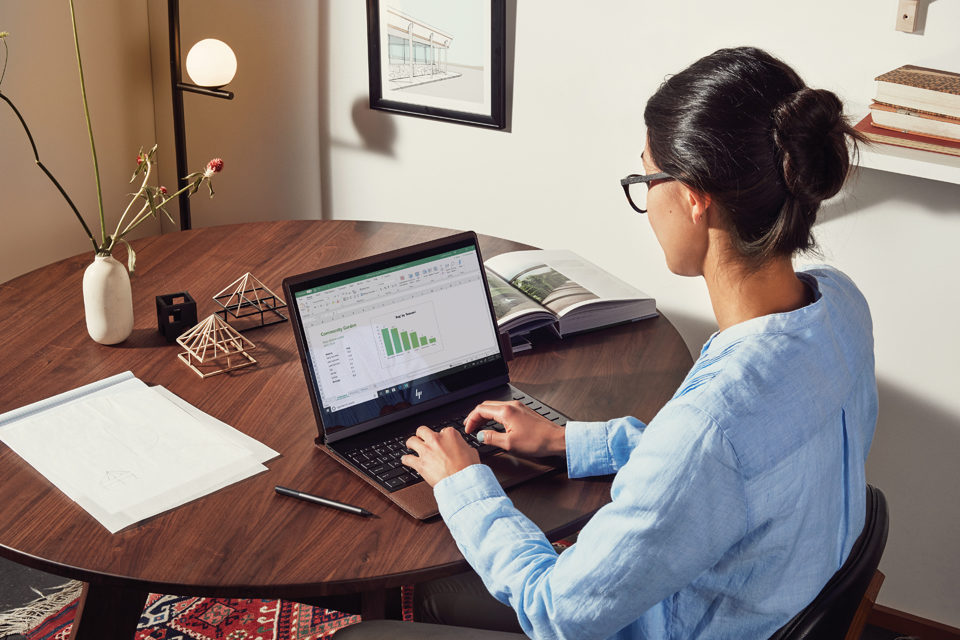 Eine Frau sitzt zu Hause an einem Tisch und arbeitet an ihrem Laptop.