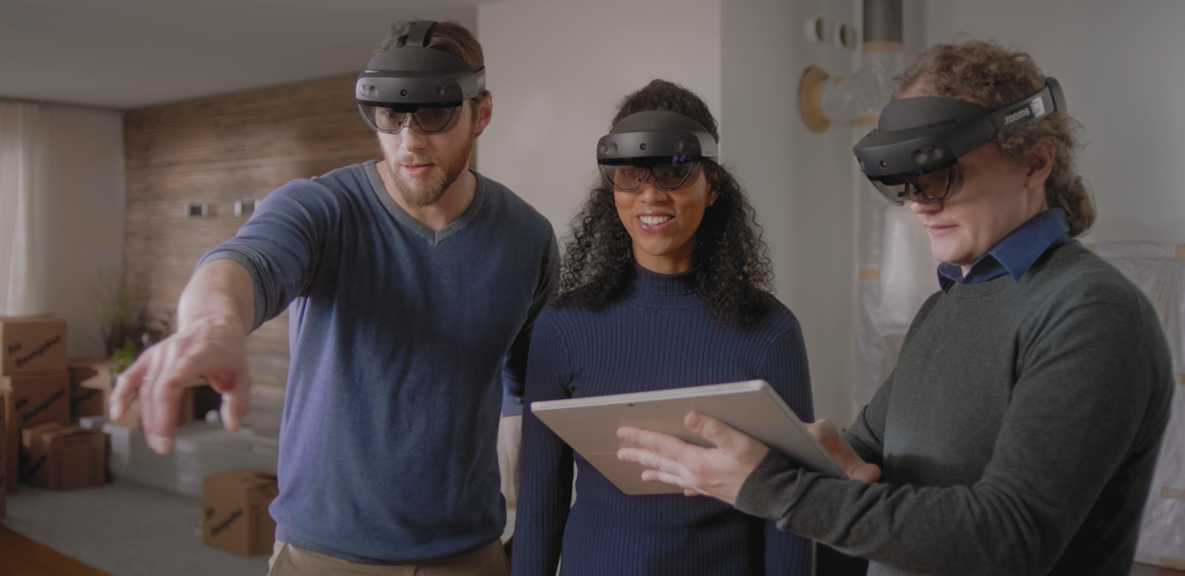 Drei Personen planen gemeinsam. Alle tragen eine Microsoft HoloLens 2, ein Mann hält ein Tablet in seiner Hand.