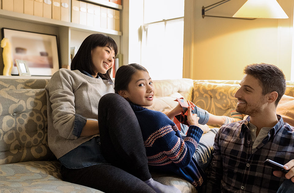 Eine Familie befindet sich zu Hause und sitzt auf dem Sofa.