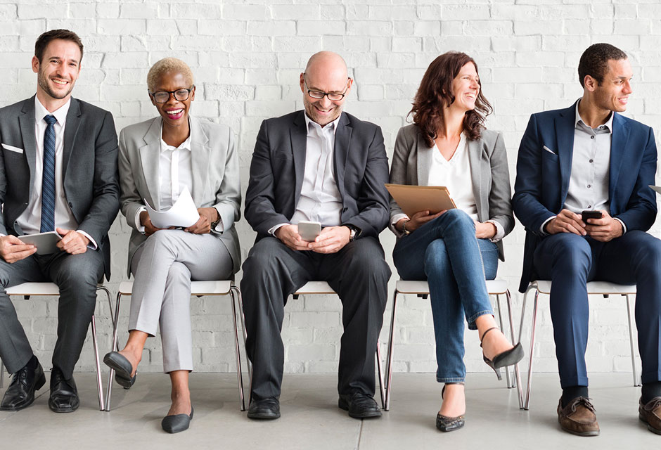 Menschen die in einer Reihe nebeneinander auf Stühlen sitzen und in diesem Fall sympathische Führungskräfte darstellen sollen