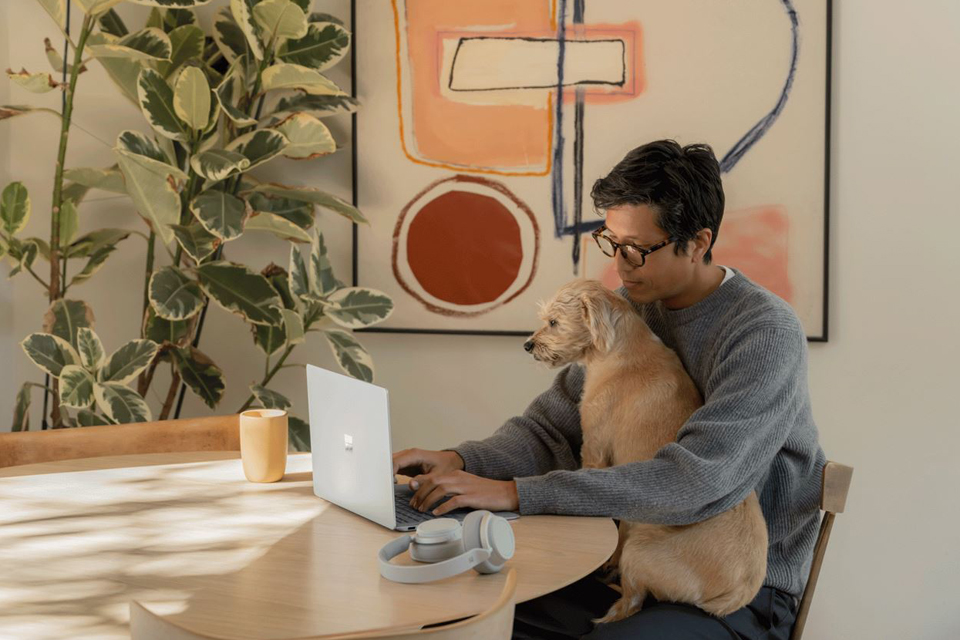 Ein Mann arbeitet mit Hund auf dem Schoß am Esstisch.