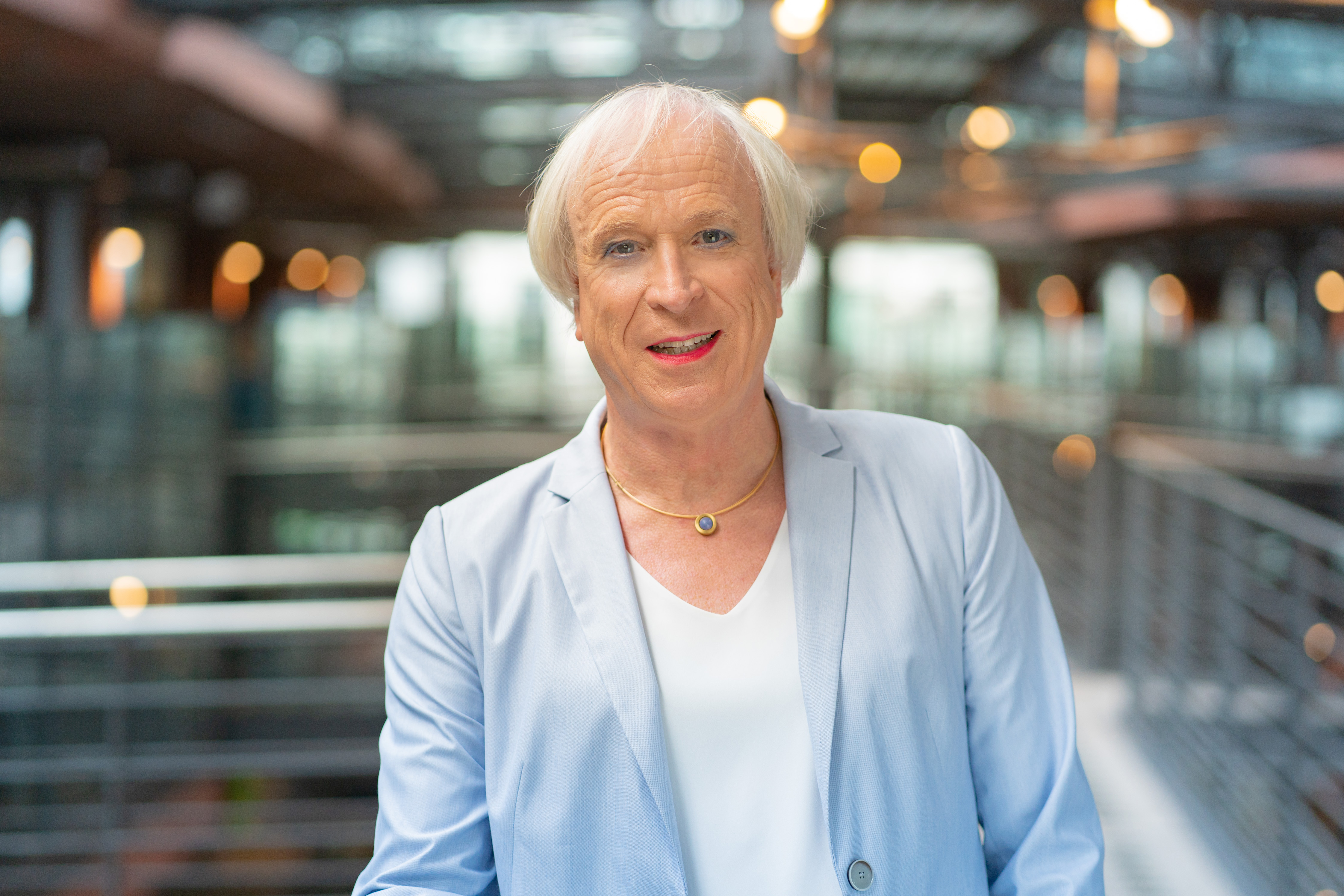 Eine Frau mit grauen Haaren lacht freundlich in die Kamera. Sie trägt eine weisse Bluse und einen hellblauen Blazer.