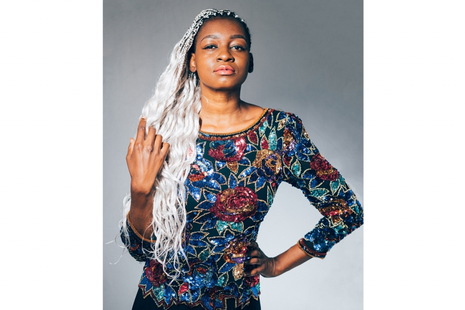 Eine junge Frau (Malonda) mit langen blonden Dreadlocks und einem bunten Pailetten-Shirt blickt selbstbewusst in die Kamera